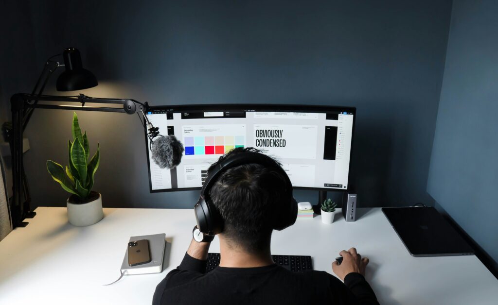 Person wearing headphones working at a minimalist desk setup with a curved monitor and podcast microphone.
